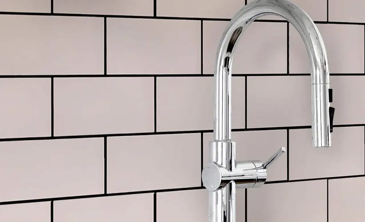 A chrome faucet arches over a wall of light pink subway tiles with smooth grout.
