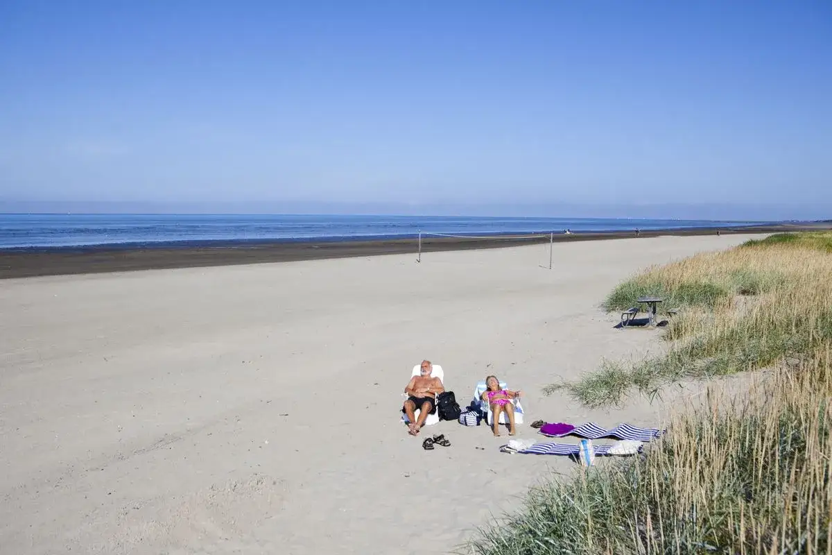 Två personer solar på stranden vid Björkäng camping. En volleybollnät står uppsatt i bakgrunden.