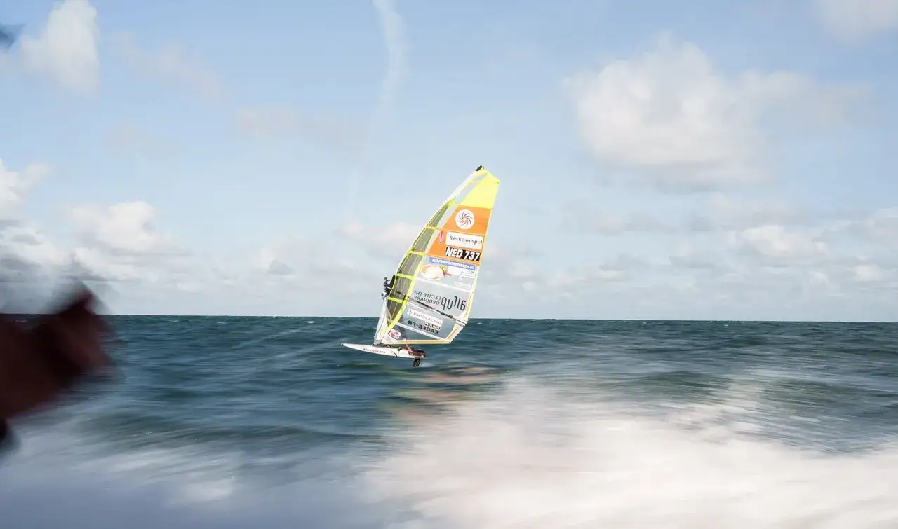 Ein Windsurfer gleitet &uuml;ber das Meer. Das bunte Segel mit der Aufschrift 