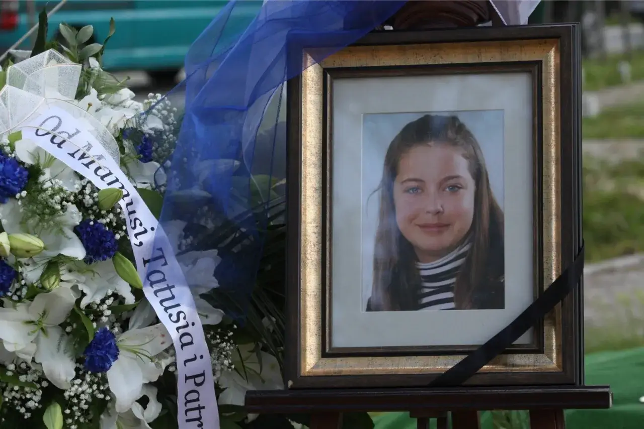 Wspomnienie Izabeli Strzałkowskiej. Uśmiechnięta młoda dziewczyna na zdjęciu, obok bukiet białych lilii i niebieskich chabrów, ozdobiony wstęgą z napisem