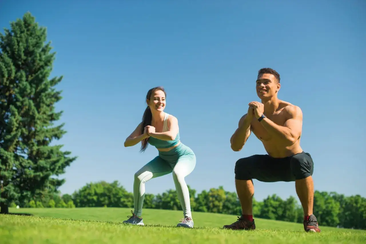 Pareja haciendo sentadillas al aire libre, un ejercicio clave para eliminar grasa abdominal y tonificar el cuerpo.