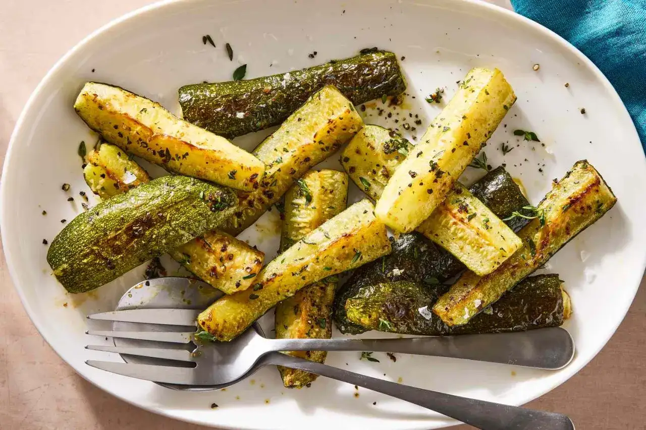Zucchine al forno semplici light, tagliate a bastoncini e condite con erbe aromatiche e pepe nero, servite su un piatto bianco con forchetta e coltello.