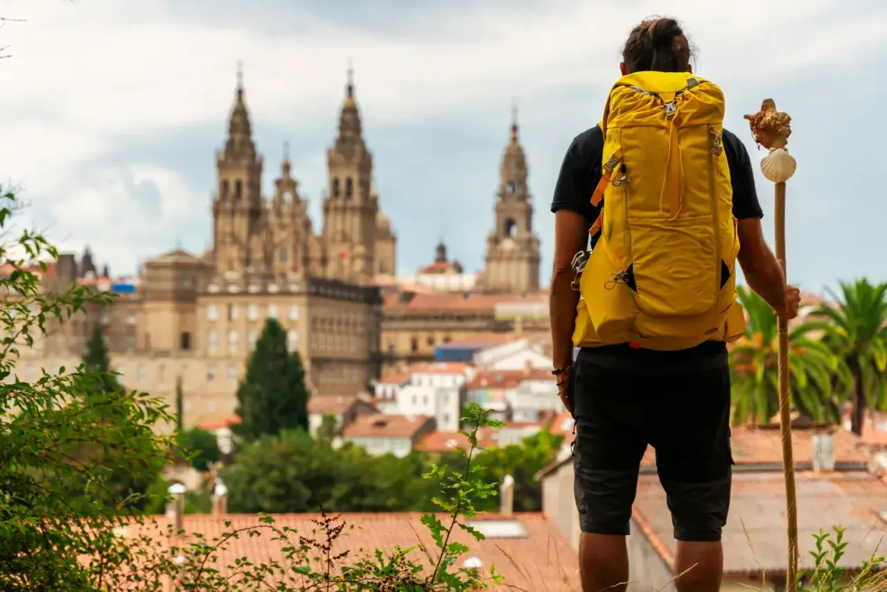 Pielgrzym z żółtym plecakiem i laską przed katedrą w Santiago. To inspiracja, jak przygotować się do przejścia trasy Camino de Santiago z Polski.