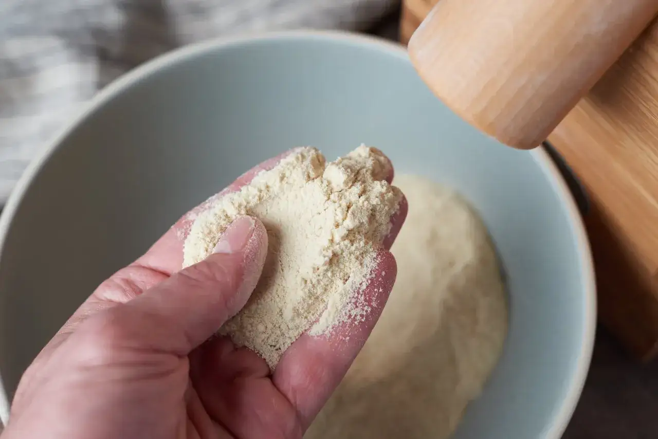 Feines Mehl in der Hand, bereit zum Backen. Ein Nudelholz liegt daneben, bereit, um Teig auszurollen.
