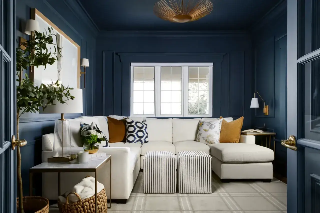 Gemütliches Wohnzimmer mit einem weißen Ecksofa, Akzentkissen in blau nuancen und einem Teppich.