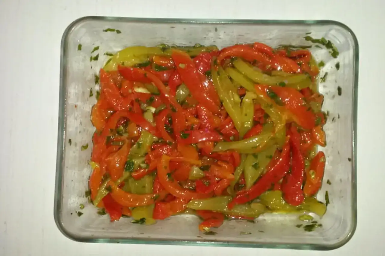 Poivrons marinés rouges et verts, coupés en lanières, dans un plat en verre, parsemés de persil frais. Un délice pour accompagner vos plats.