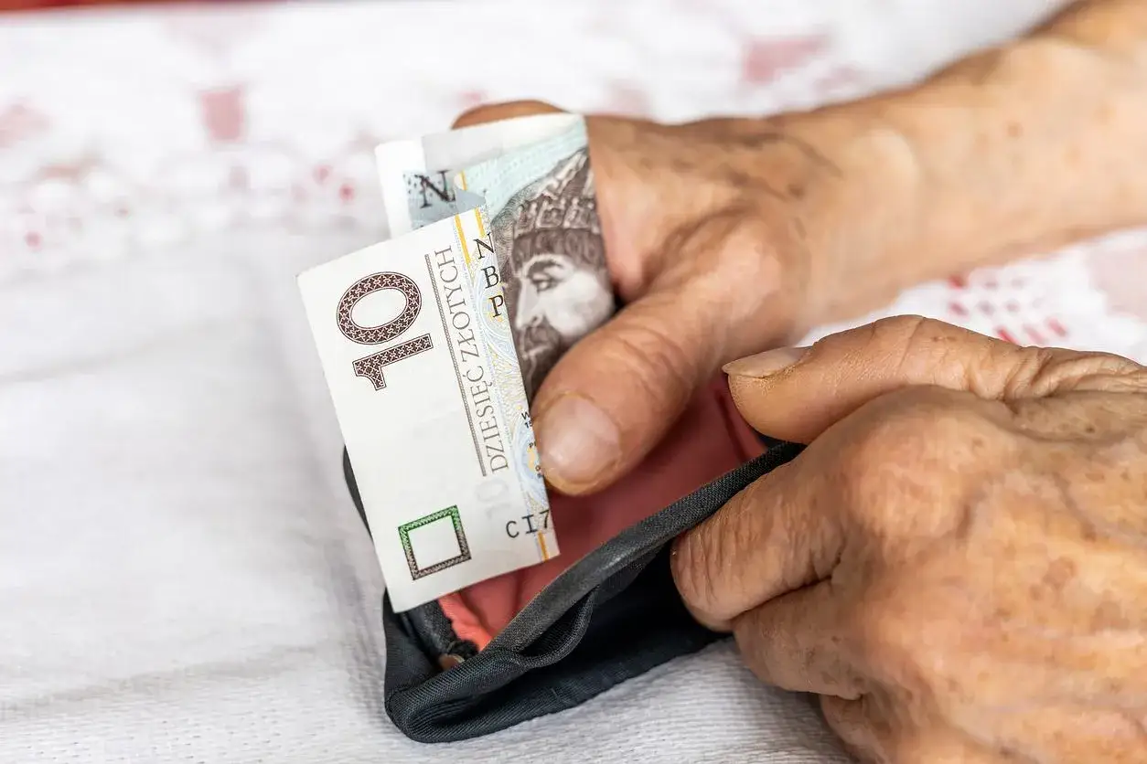 Dłonie starszej osoby chowają banknot 10 zł do portmonetki. Czekamy, kiedy wyrównają emerytury czerwcowe.