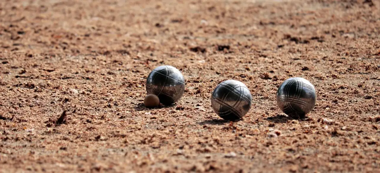 Trois boules de p&eacute;tanque m&eacute;talliques, dont une plus petite, reposent sur un terrain sablonneux. Le poids boule est bien visible.