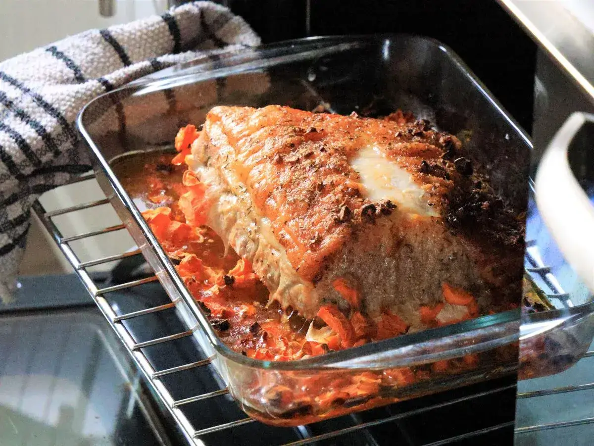 Super delikatny i soczysty schab gotowany w naczyniu żaroodpornym, otoczony pomarańczowymi warzywami.