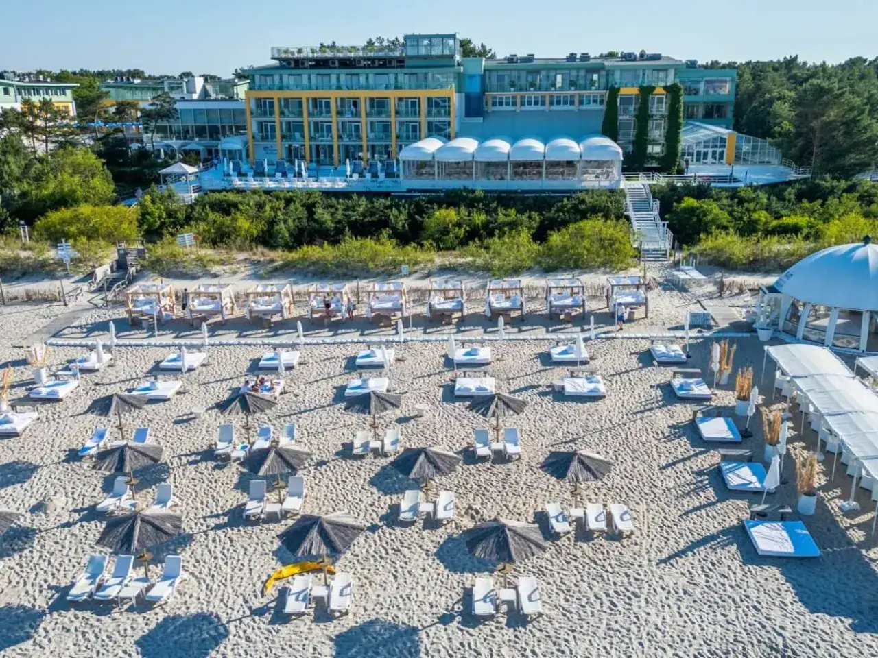 Piękna plaża z leżakami i parasolami, gdzie czuć orzeźwiającą bryzę. W tle hotel z widokiem na morze.