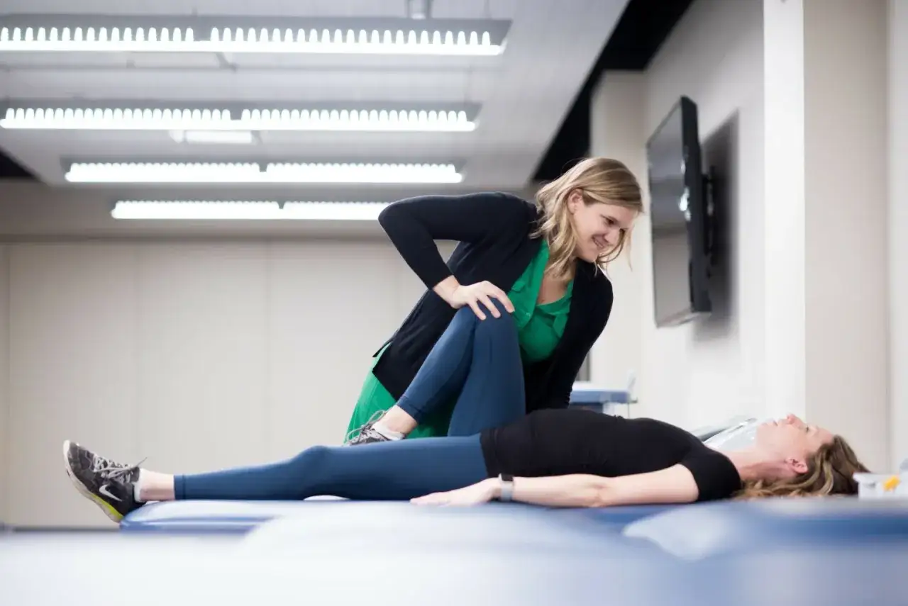 Eine Trainerin &uuml;bt bei einer &Uuml;bung, die Teil ihrer Athletiktrainer Ausbildung ist, Druck auf das Bein einer liegenden Frau aus.