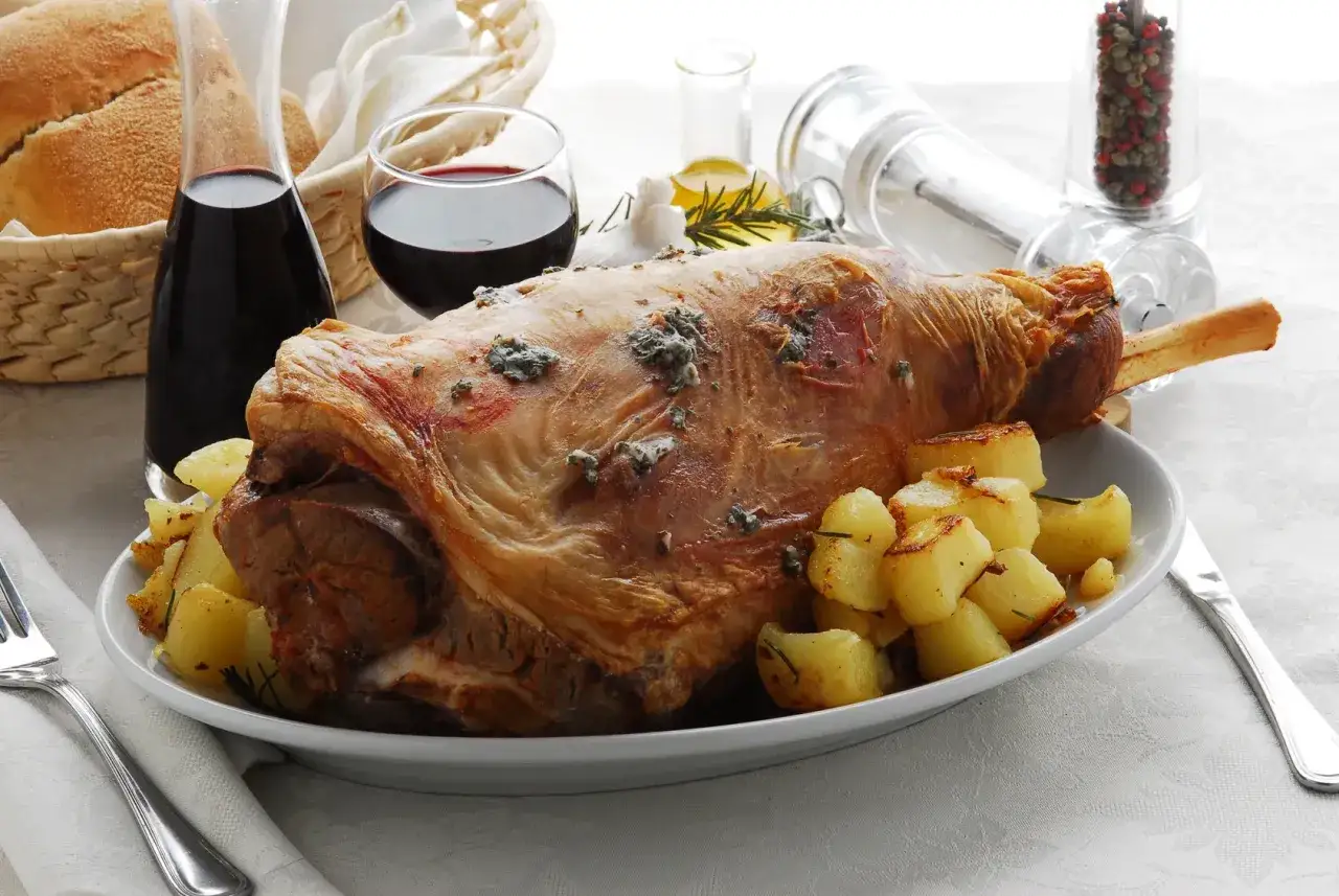 Arrosto di agnello dorato con patate, vino rosso e pane, un classico dei piatti pasquali.