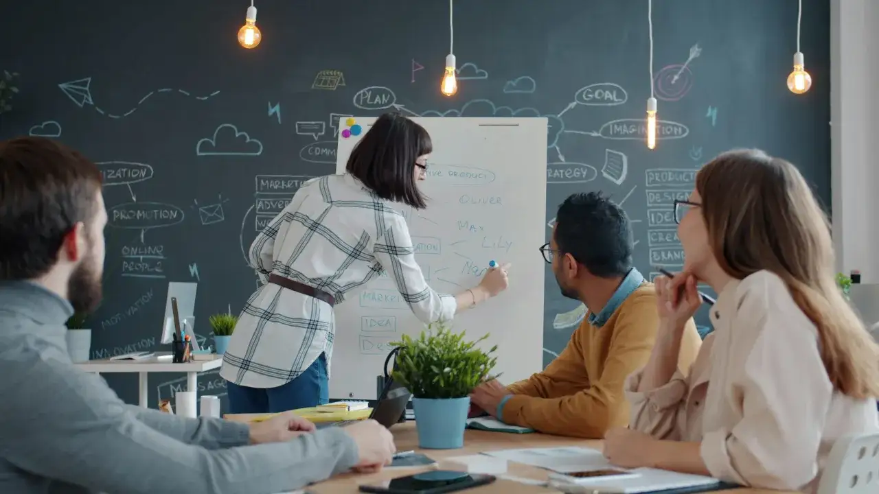 A team brainstorms ideas, fostering innovation and employee engagement. A woman writes on a whiteboard with a team observing.