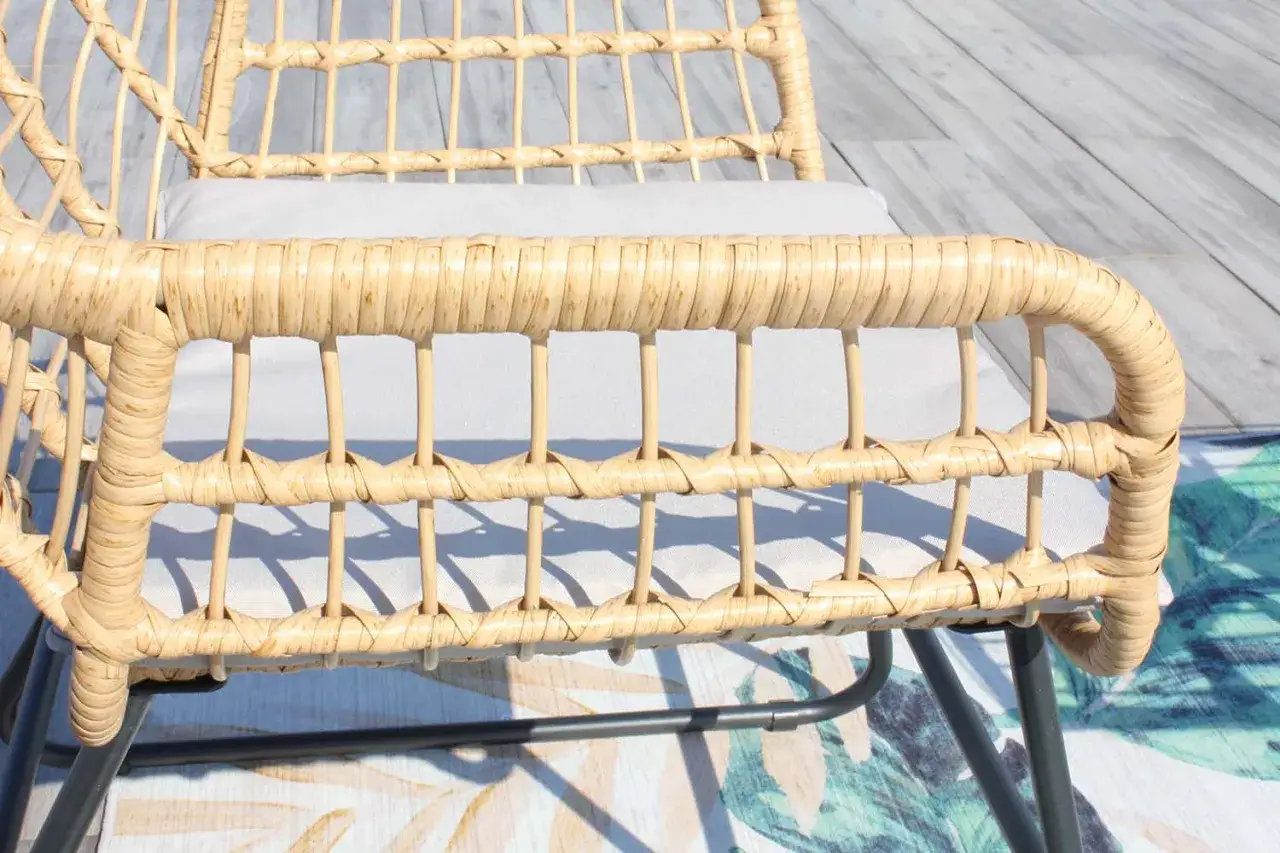 D&eacute;tail d'un fauteuil en rotin tress&eacute;, pr&ecirc;t pour son entretien. Le coussin gris clair est visible sous l'assise.