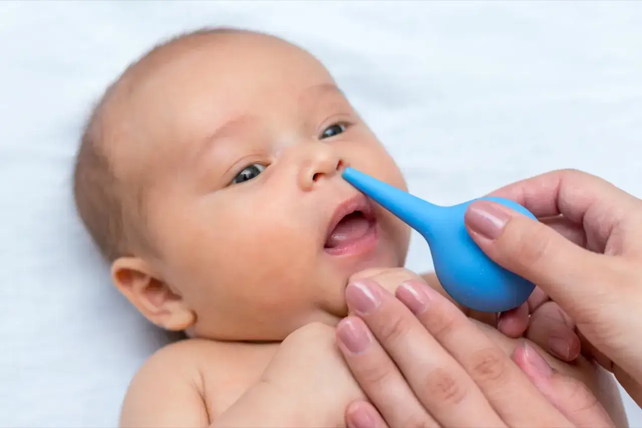 Mani delicate usano un aspiratore nasale blu per alleviare il raffreddore neonato.