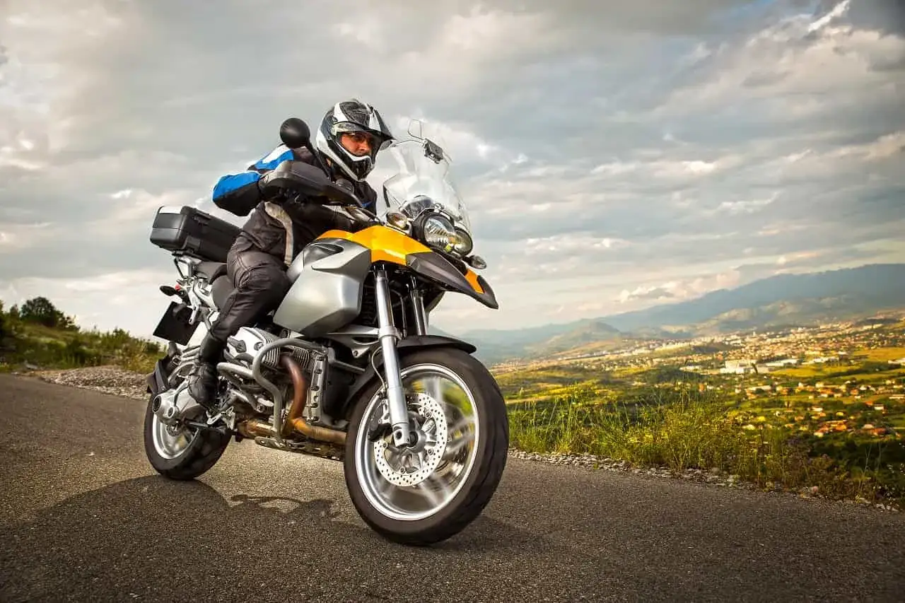 Motocyklista w kasku i kurtce jedzie drogą z widokiem na miasto w oddali. Przygotowuje się do rejestracji motocykla z zagranicy.