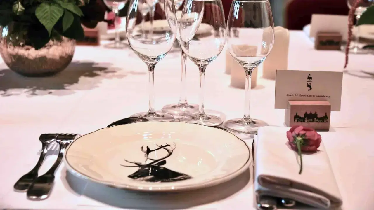 Une table dressée pour un dîner élégant, avec une assiette ornée d'un cerf, des verres à vin et une carte de visite. L'art de poser les couverts à la française est respecté.