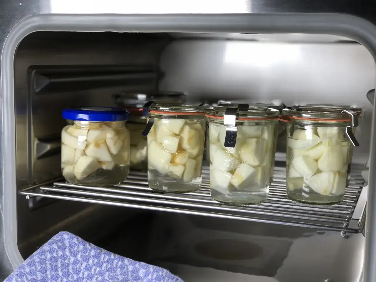 Gl&auml;ser mit Apfelst&uuml;cken stehen auf einem Rost im Dampfgarer. Das Einkochen im Dampfgarer ist eine schonende Methode zur Konservierung von Obst.