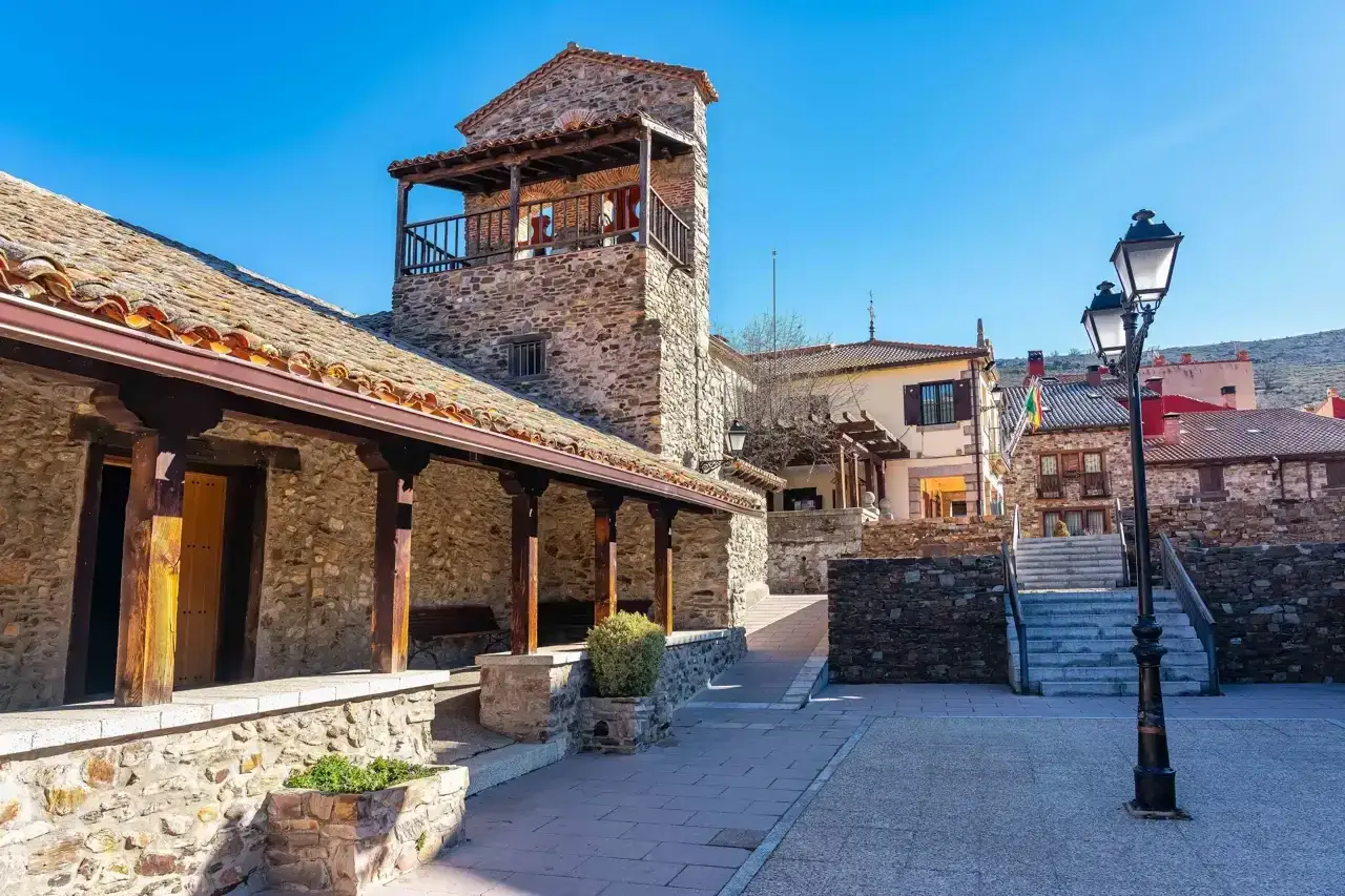 Puebla de la Sierra que ver: plaza con torre de piedra, soportales de madera y casas tradicionales bajo un cielo azul.