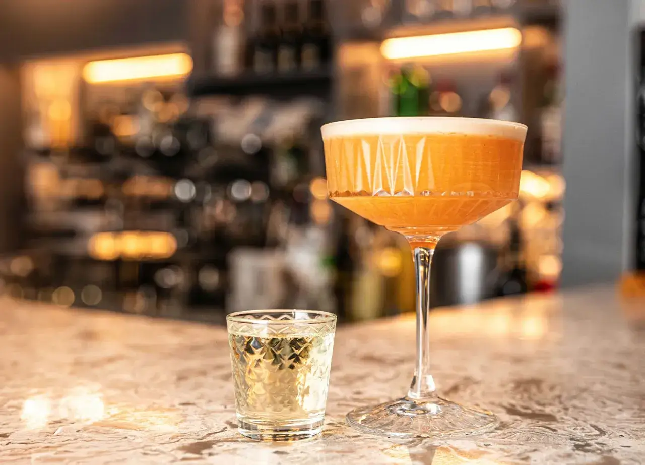 Elegancki kielich z pomarańczowym drinkiem i kieliszek z wódką waniliową na barze.