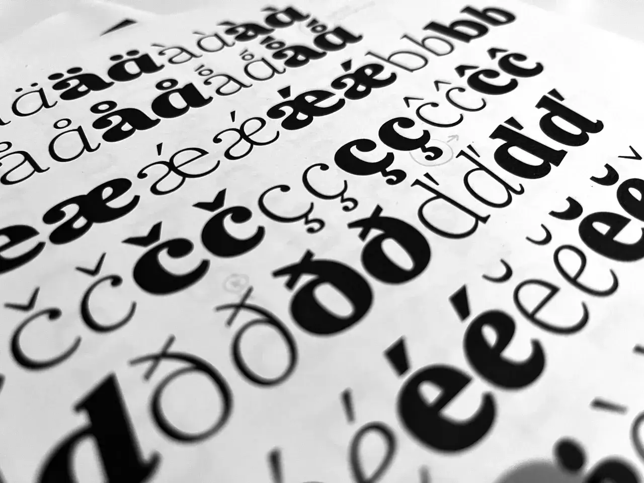Black and white letters, including accented characters, are displayed on paper, hinting at the process of how to create a font in Illustrator.