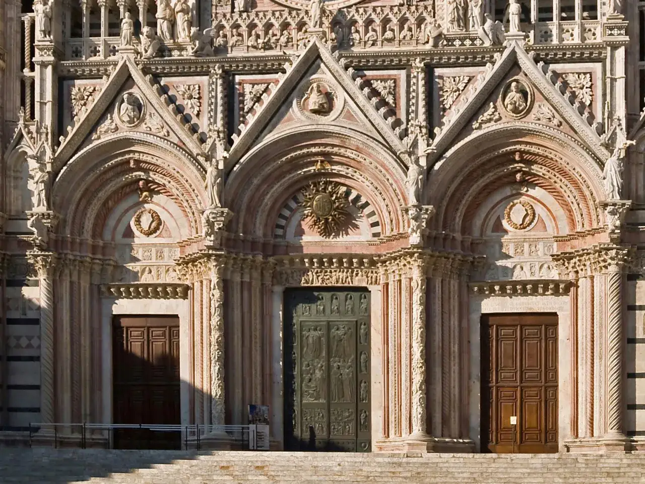 Dettaglio della facciata del **Siena Cathedral** con tre portali, decorazioni scultoree e marmi policromi.