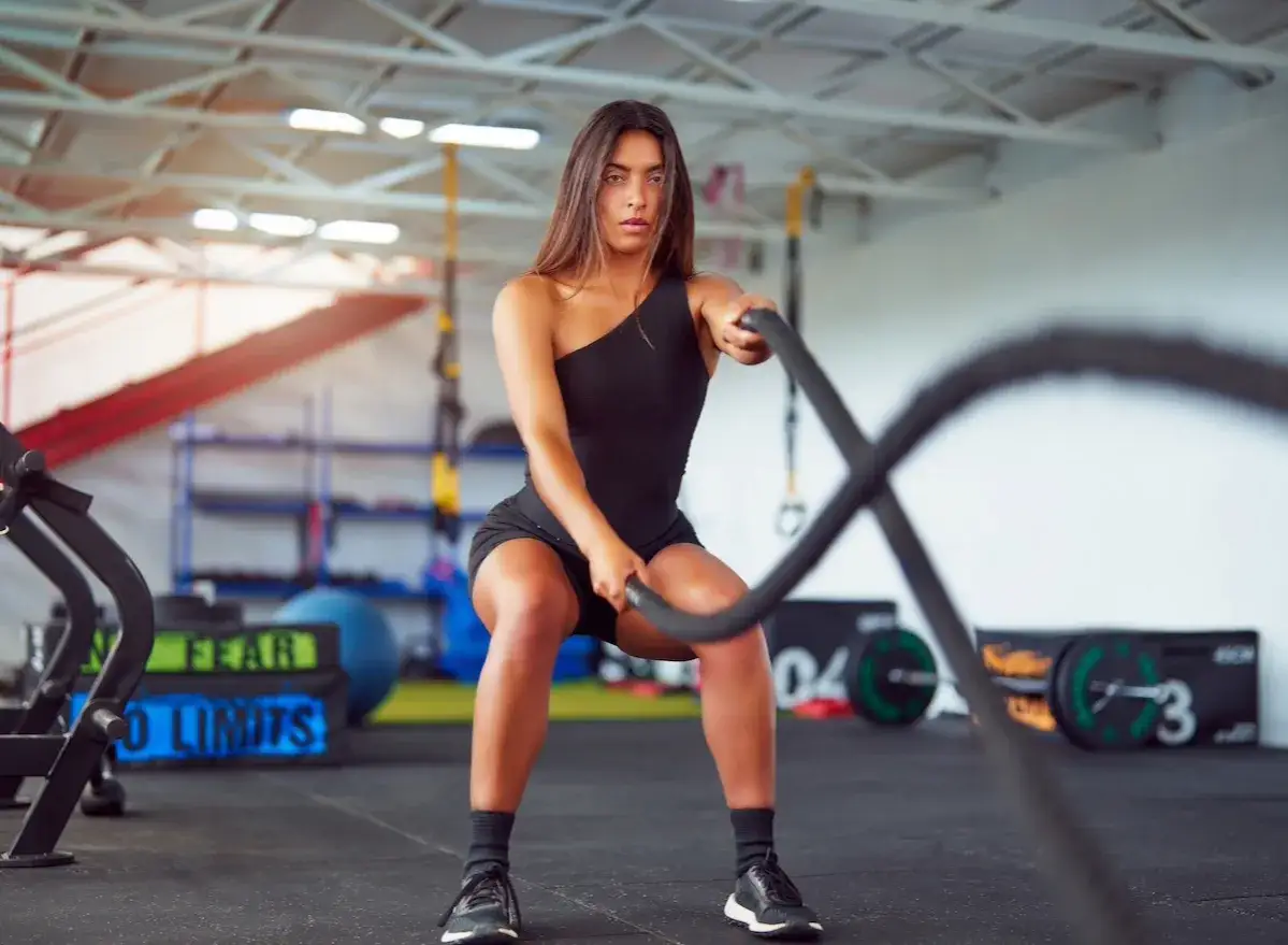 Donna determinata esegue un allenamento **hiit per dimagrire** con le battle ropes in palestra, concentrata sul movimento.