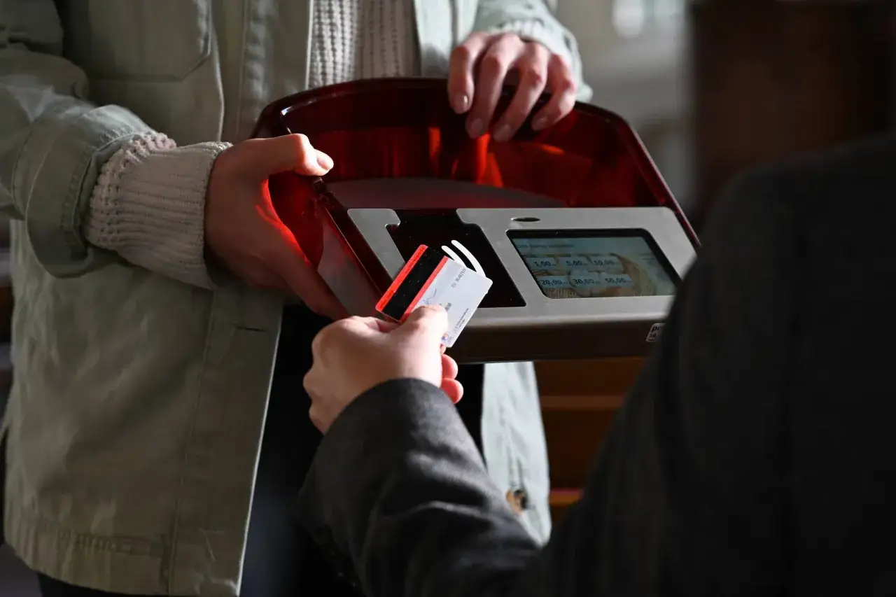 Gabe beim Gottesdienst: Eine Person h&auml;lt eine Karte an ein Leseger&auml;t, um einen Betrag zu spenden.