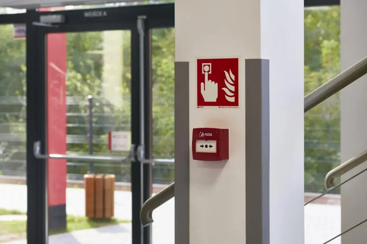 Czerwony przycisk alarmowy i znak informujący o pożarze na słupie. To część systemu ppoż. w budynku.