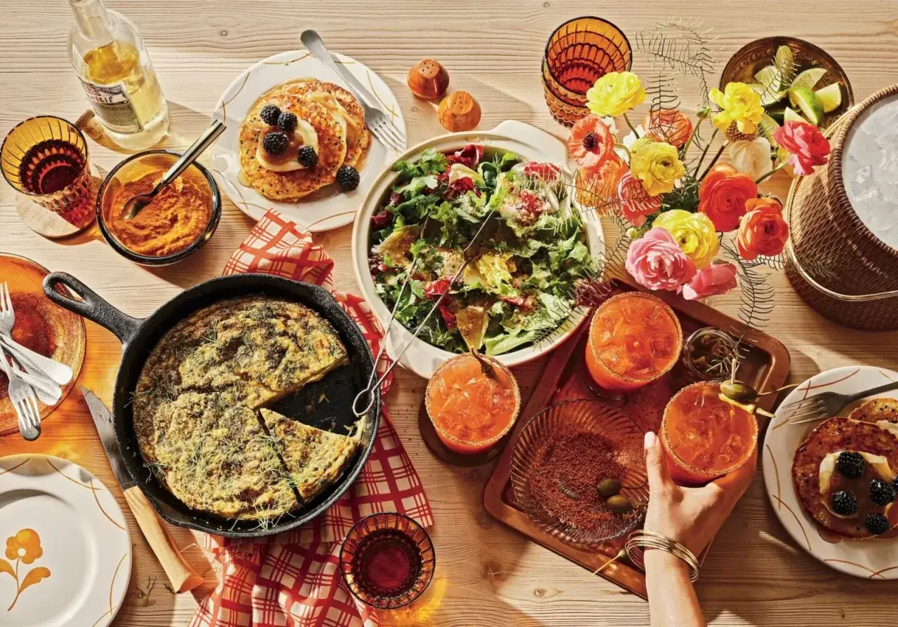 En lyxig frukost med pannkakor, frittata, sallad och drinkar. Blommor och solljus skapar en h&auml;rlig st&auml;mning.