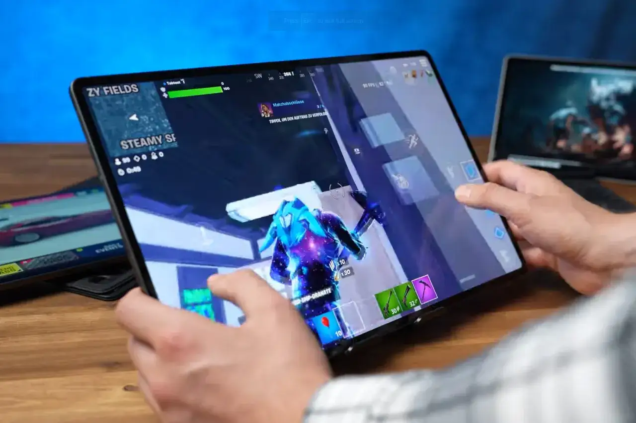 Gracz gra w Fortnite na tablecie, szukając najlepszych gier na tablet. W tle widać inny tablet z grą wyścigową.