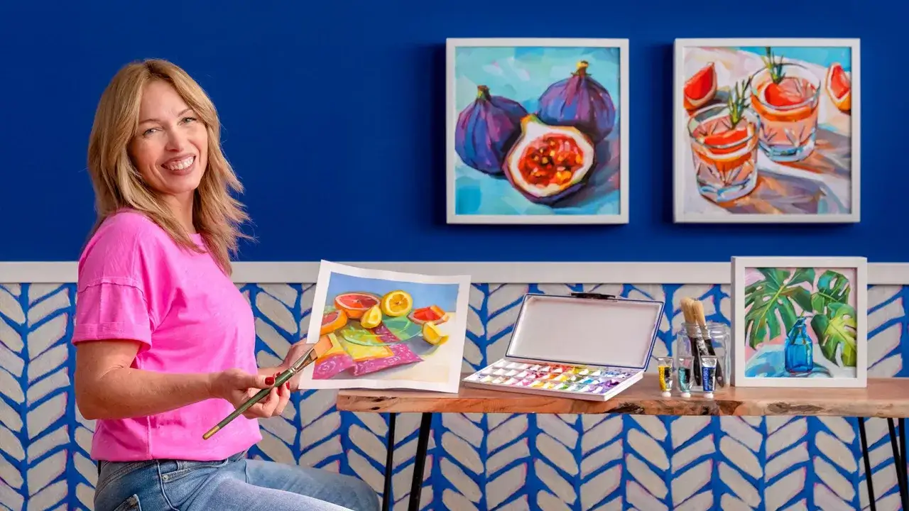 Artiste souriante tenant un pinceau, prête à peindre à la gouache sur toile. Des natures mortes colorées ornent le mur bleu vif.