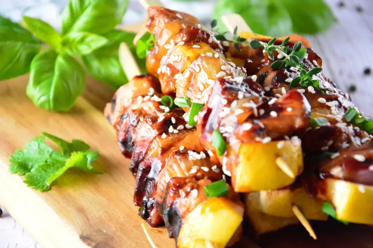 Pyszne yakitori z kurczaka w sosie teriyaki, posypane sezamem i szczypiorkiem, na drewnianej desce z bazylią.
