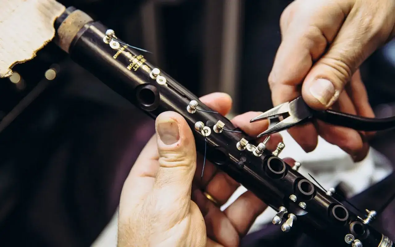 Réparation d'un clarinette Buffet Crampon à Mantes. Un artisan ajuste délicatement les clés avec une pince.