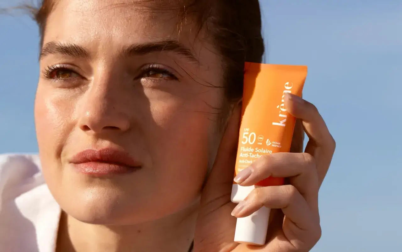 Une femme tient un tube de crème solaire SPF 50. L'effet crème solaire sur la peau est visible, protégeant du soleil.