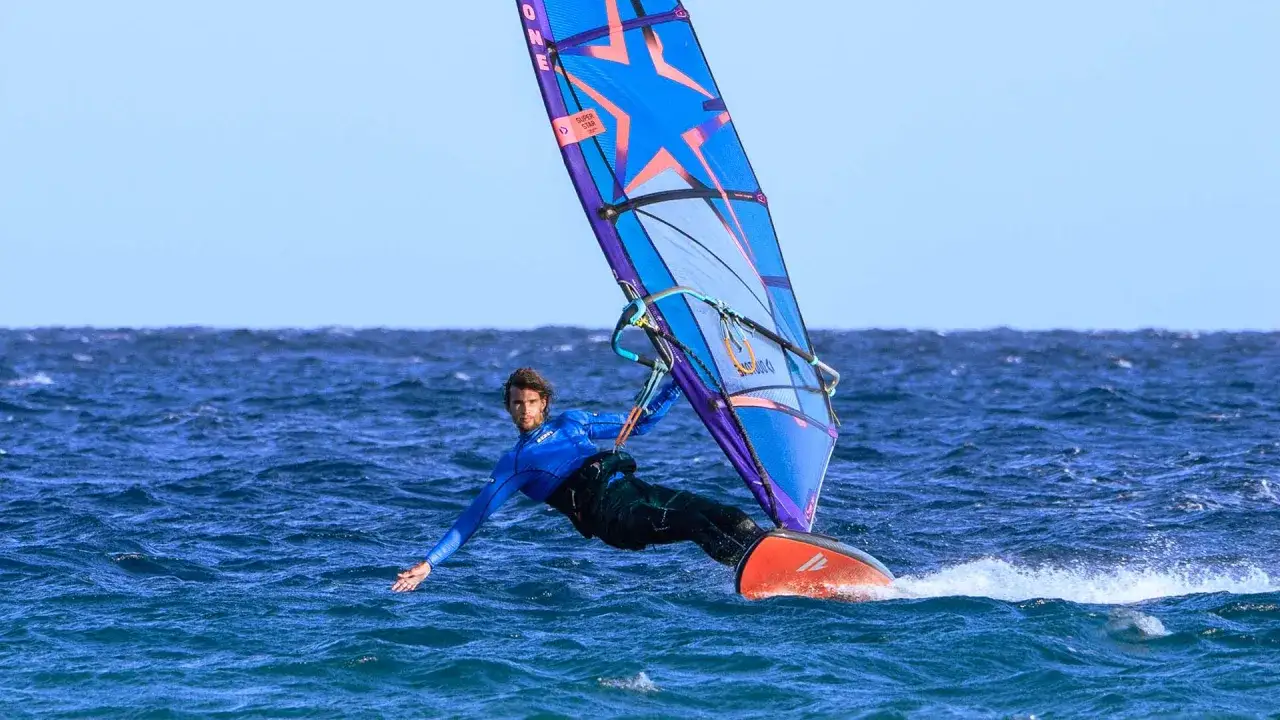 Windsurfer in Aktion vor Costa Calma, Fuerteventura. Der Mann im blauen Neoprenanzug gleitet über das Meer, die bunte Segel über ihm.