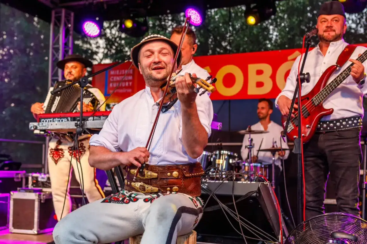 Baciary jak się bawią ludzie na scenie, grając na skrzypcach, basie i akordeonie.