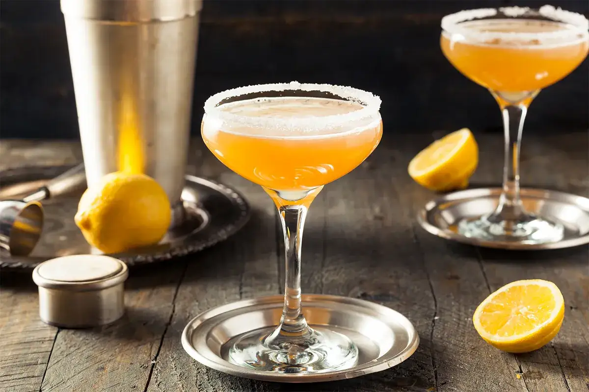 Orzeźwiający drink z cointreau, ozdobiony cukrowym rantem, z cytryną i shakerem na drewnianym stole.