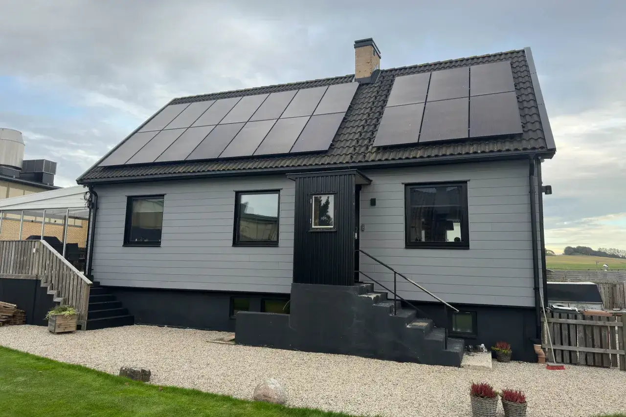 Ett ljusgrått hus med solpaneler på taket. En mörk entré med trappa leder upp till huset.