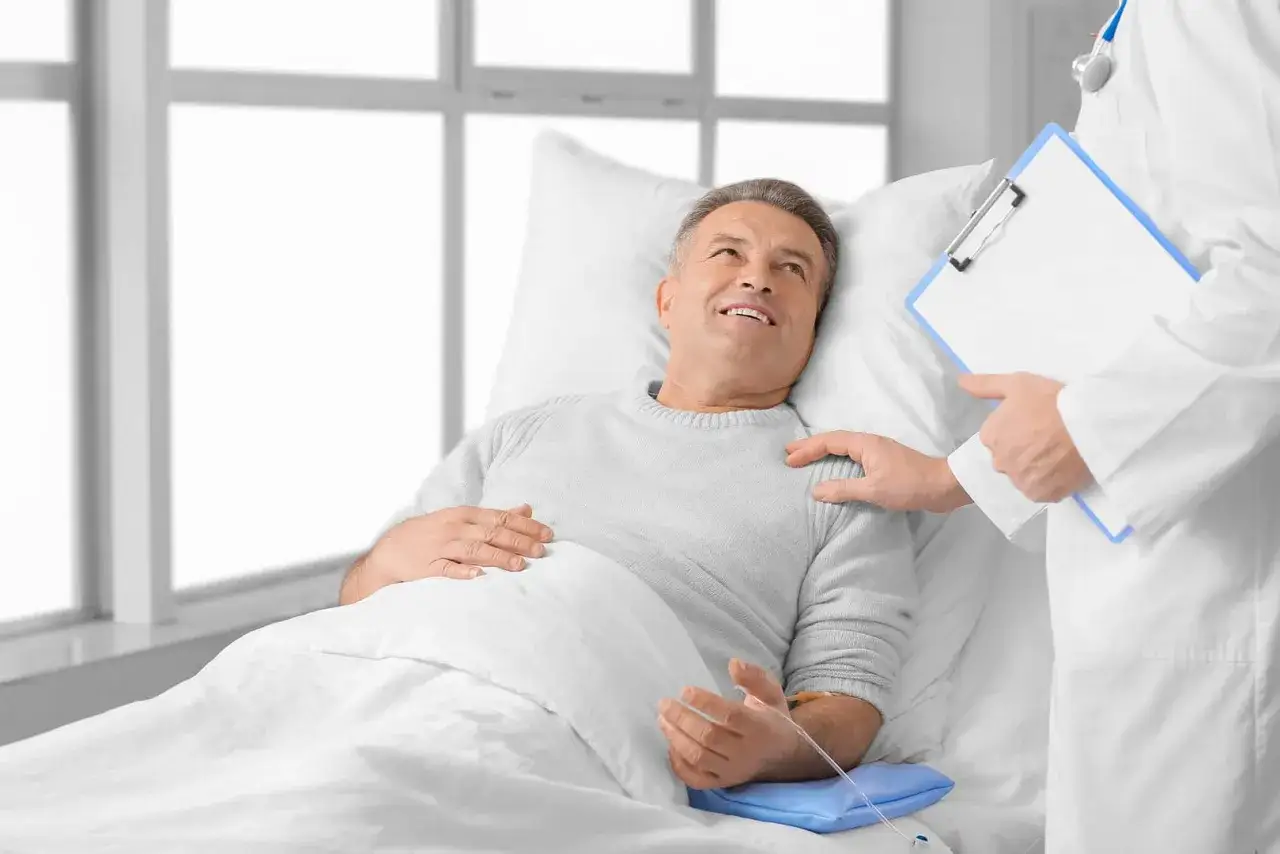 Uśmiechnięty pacjent w łóżku szpitalnym słucha lekarza o najnowszych lekach na prostatę.