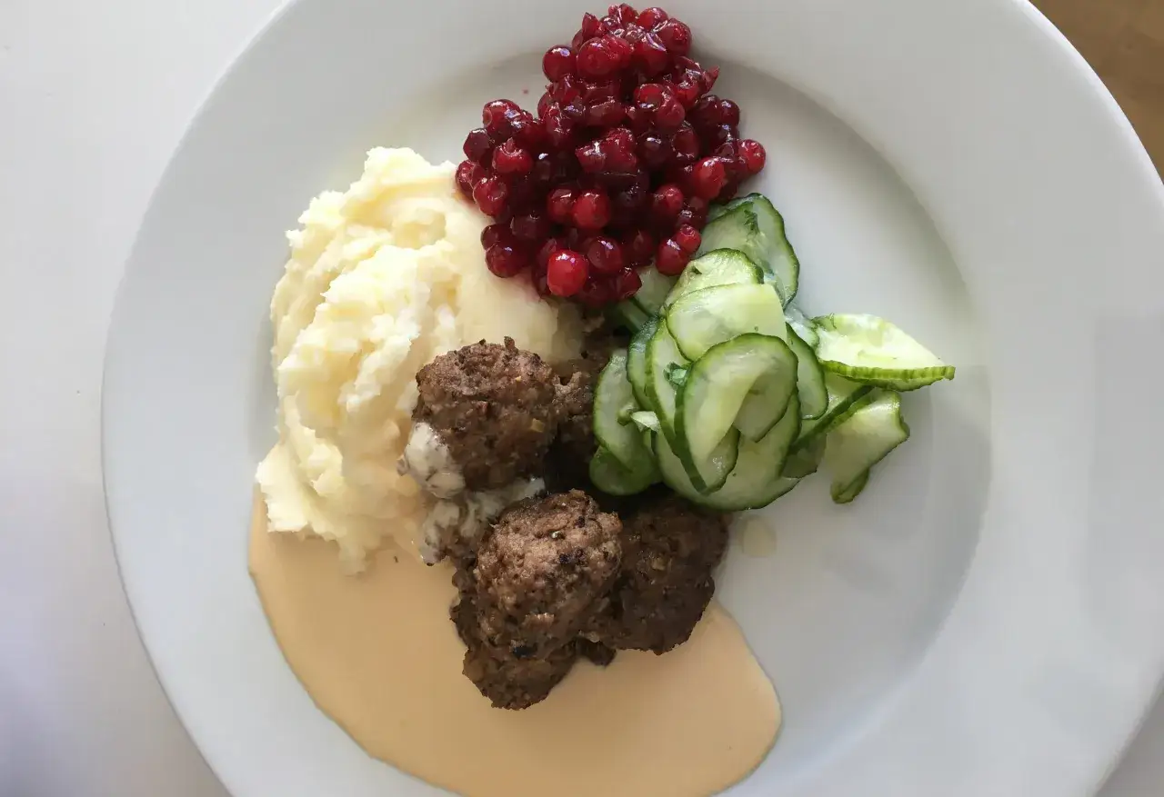 Köttbullar med potatismos, lingon och gurksallad, serverat med en krämig brunsås utan grädde.