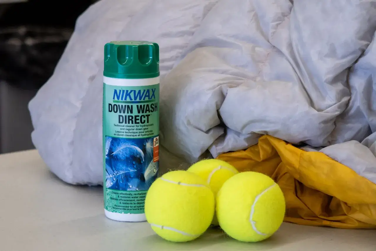 Butelka Nikwax Down Wash Direct i trzy piłki tenisowe obok śpiwora. To wszystko, czego potrzebujesz, by dowiedzieć się, jak prać śpiwór.