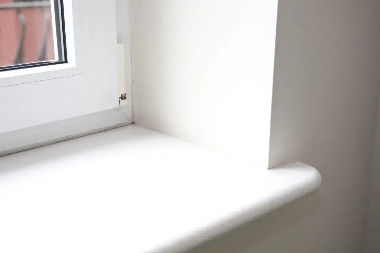 Biały parapet wewnętrzny w bloku, gotowy do montażu po wymianie.