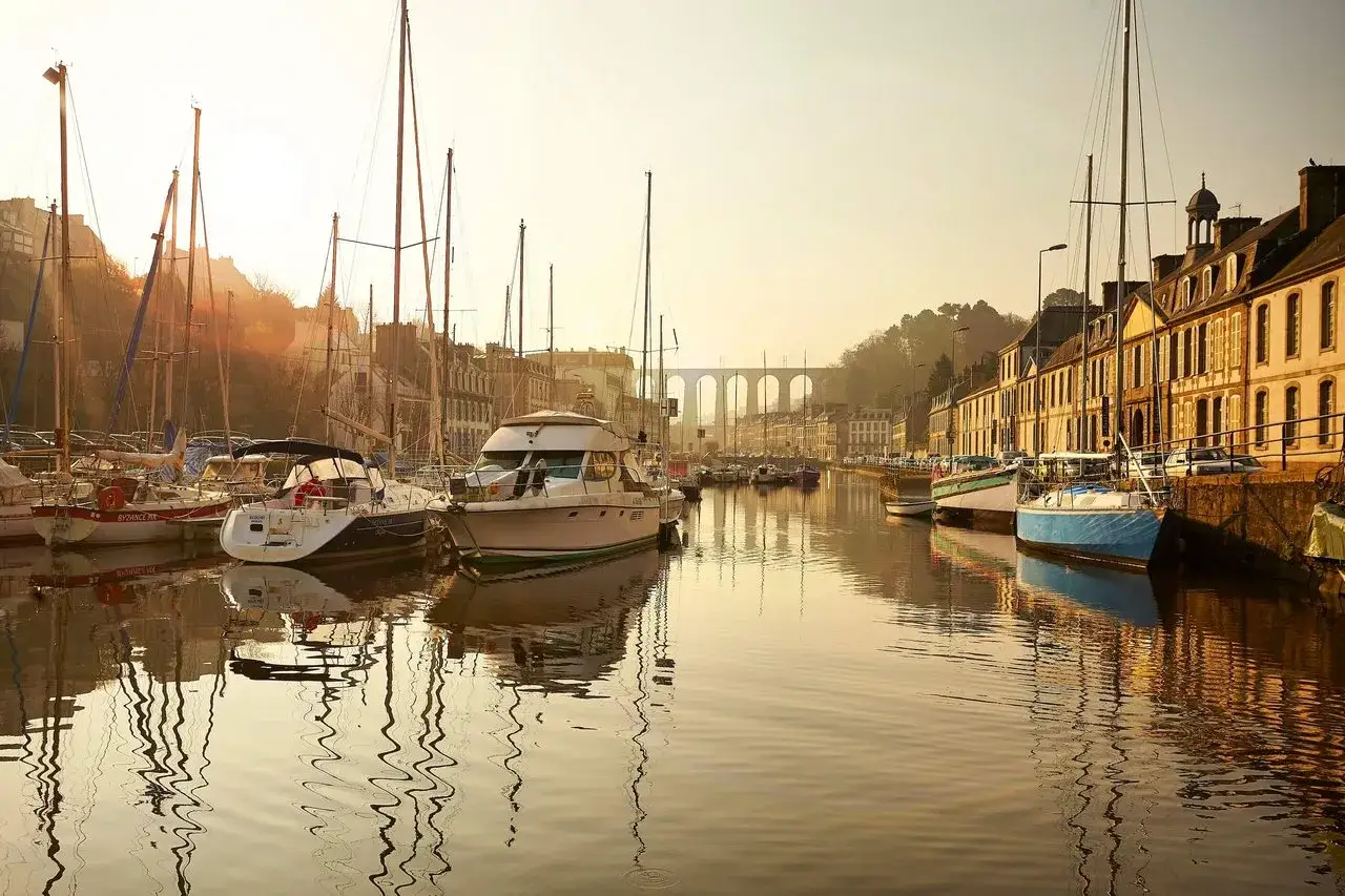 Matin paisible dans le port de Morlaix, avec des voiliers et des bateaux à moteur amarrés. Le viaduc se dresse au loin. Idéal pour savoir que faire à Morlaix.