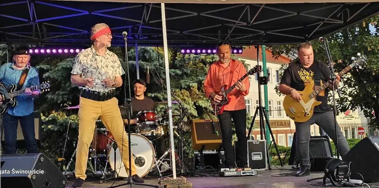 Zespół Sławka Wierzcholskiego gra na scenie. Wokalista w czerwonej opasce, gitarzyści i perkusista tworzą energetyczną atmosferę.