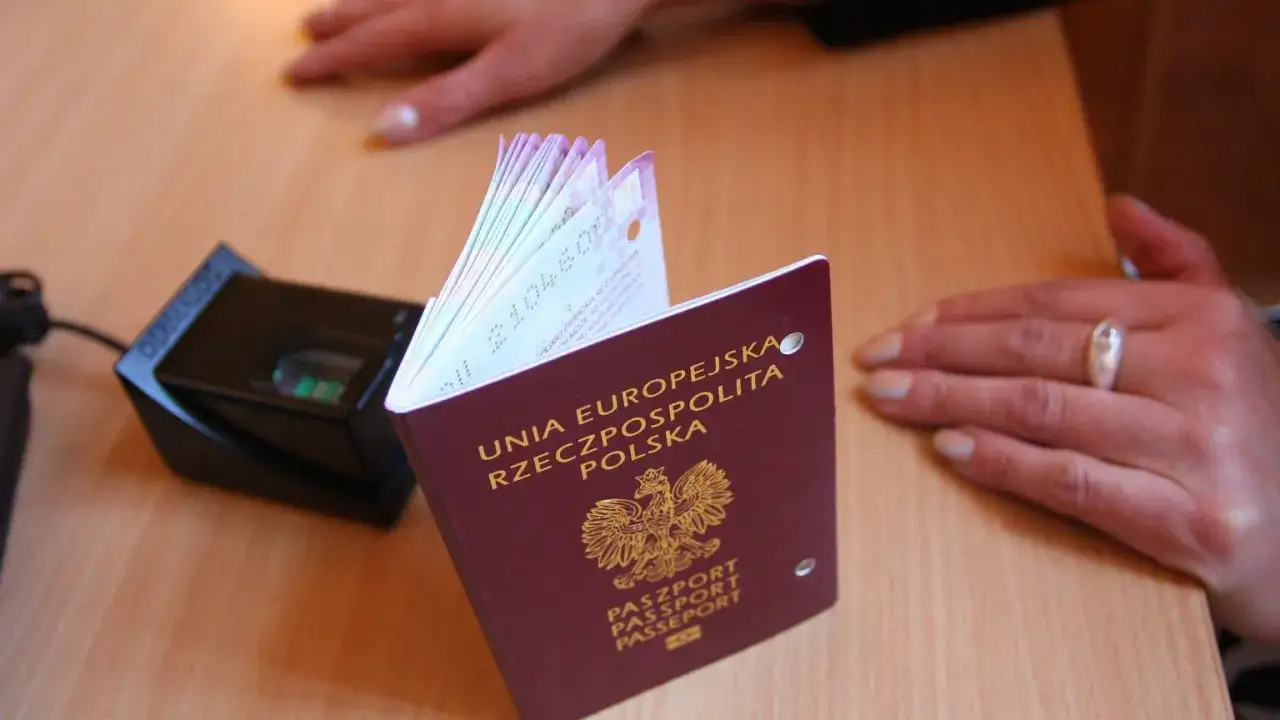 Polski paszport obok czytnika linii papilarnych. Dłoń z pierścionkiem czeka na zakończenie procedury, być może u konsula.
