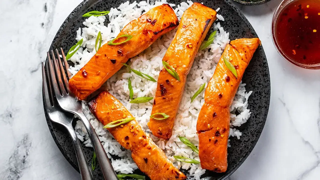 Gebratener Lachs mit einer gl&auml;nzenden, w&uuml;rzigen Sauce, serviert auf wei&szlig;em Reis und garniert mit Fr&uuml;hlingszwiebeln. Ein k&ouml;stliches Gericht, das Lust auf mehr macht.