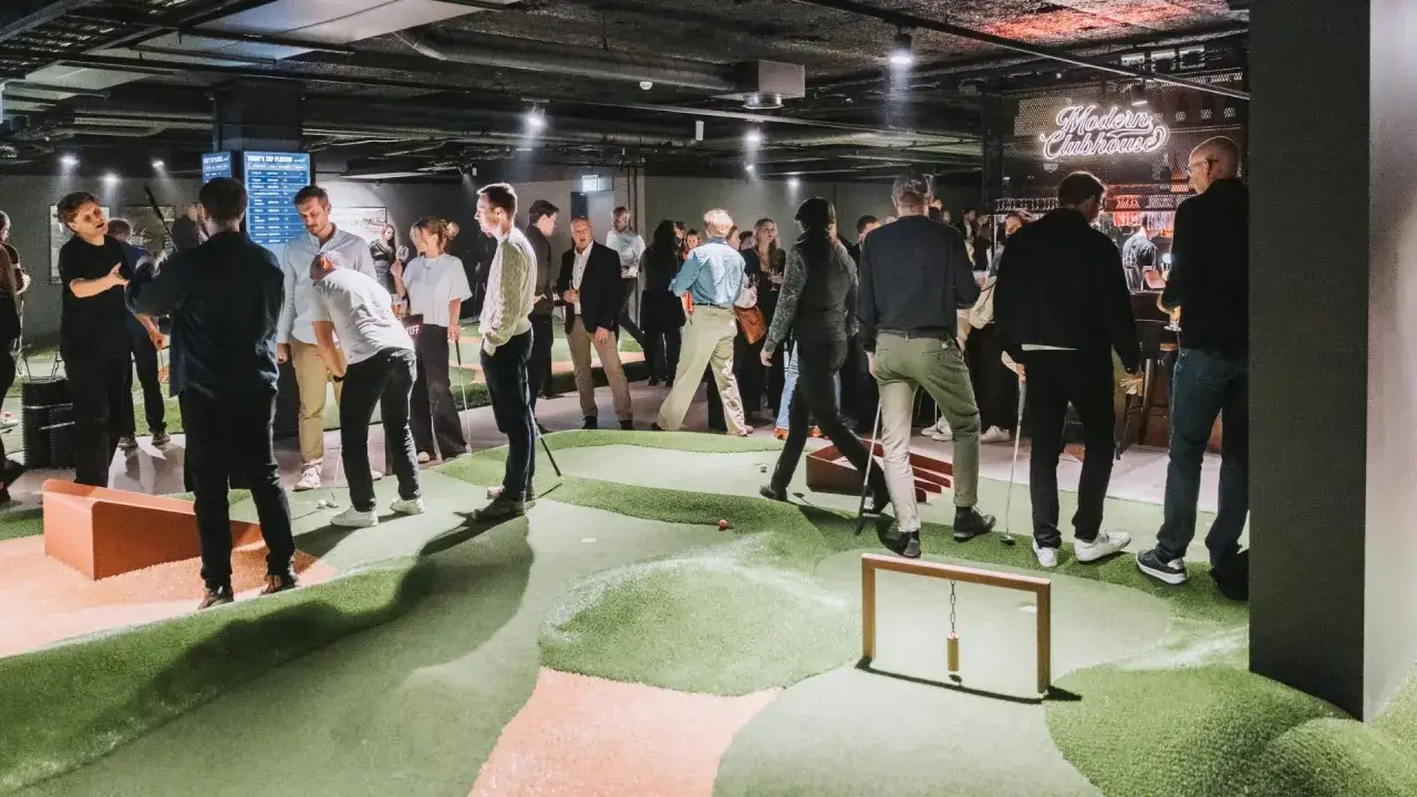 Folk spelar minigolf inomhus i Stockholm. En livlig atmosfär med många besökare som njuter av spelet.