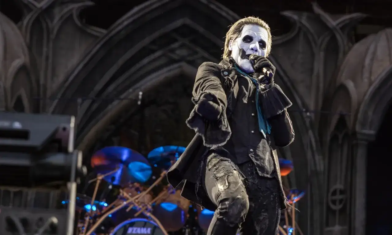 Le chanteur du groupe de musique Ghost, au maquillage blanc et noir, chante sur scène, devant une batterie bleue.