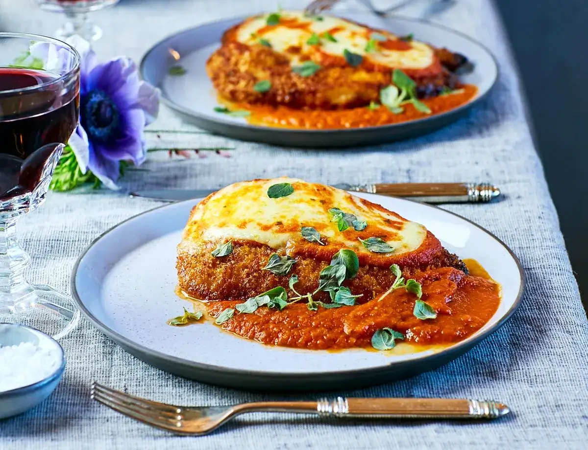 Två tallrikar med kycklingparmesan, täckt med tomatsås och smält ost. Den dubbla paneringen ger en härlig krispighet.